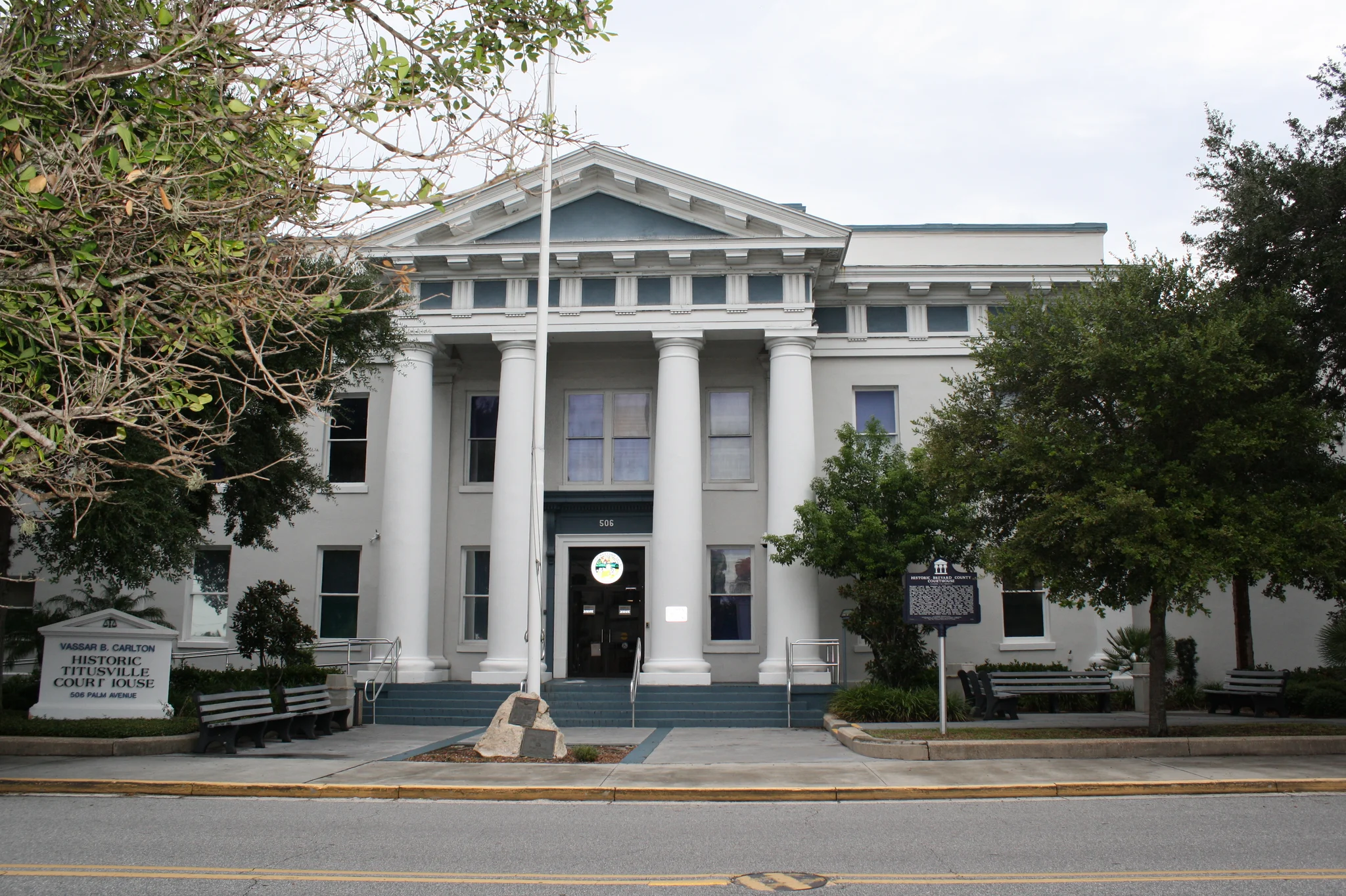 White courthouse facade with columns, front steps, trees and benches.