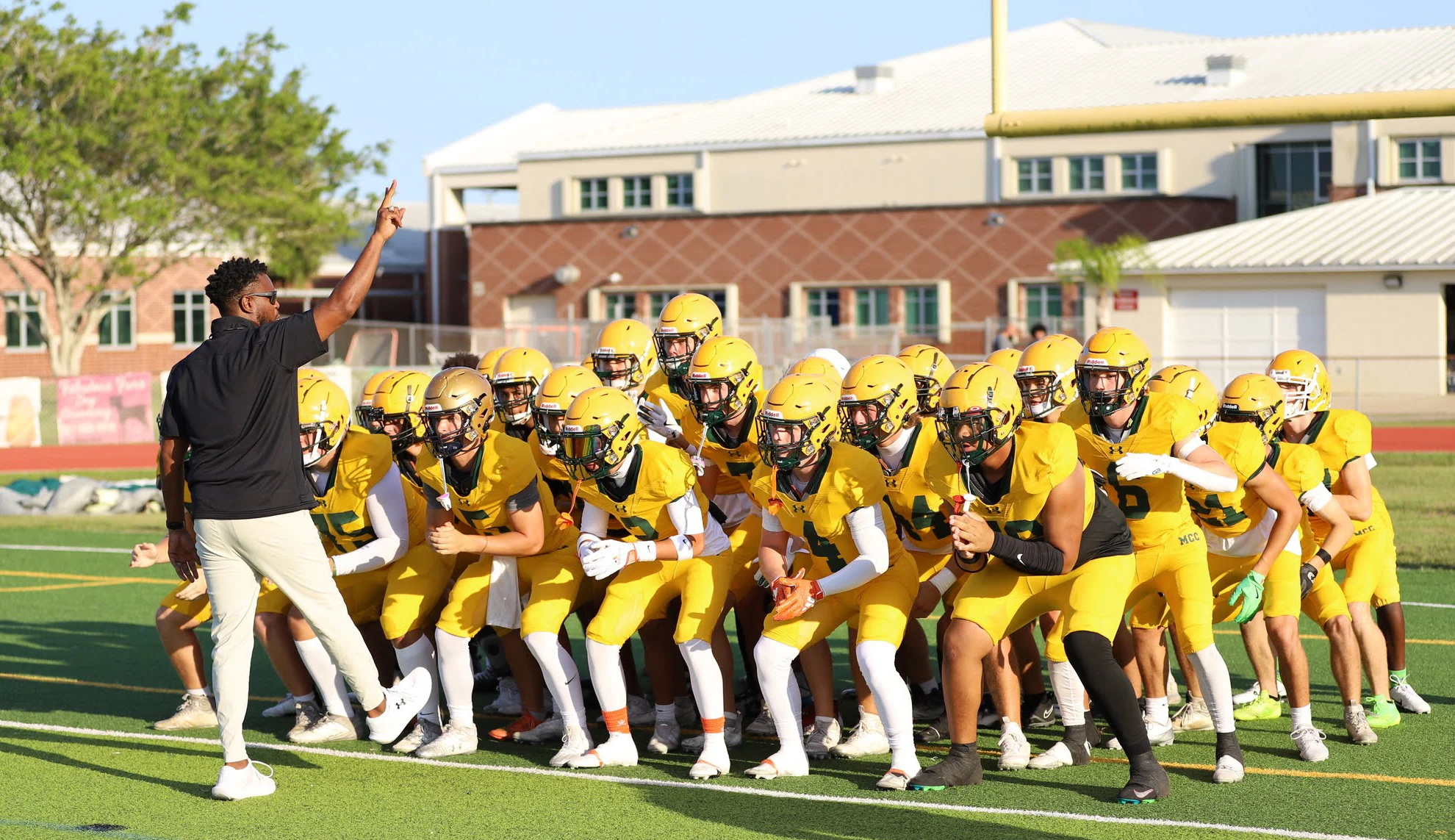 Football players in yellow uniforms gather beside a staff member on a field.