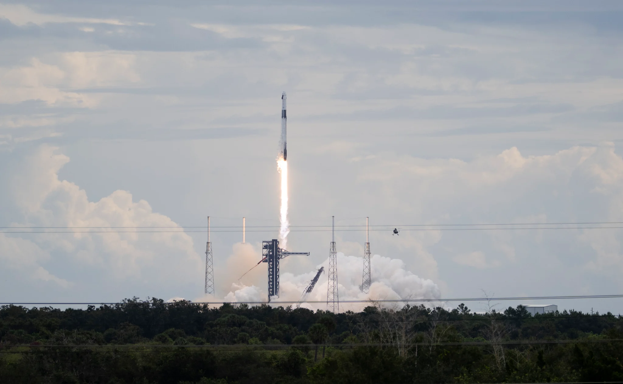 A Falcon 9 rocket carrying Dragon climbs above its launch tower on a column of flame.