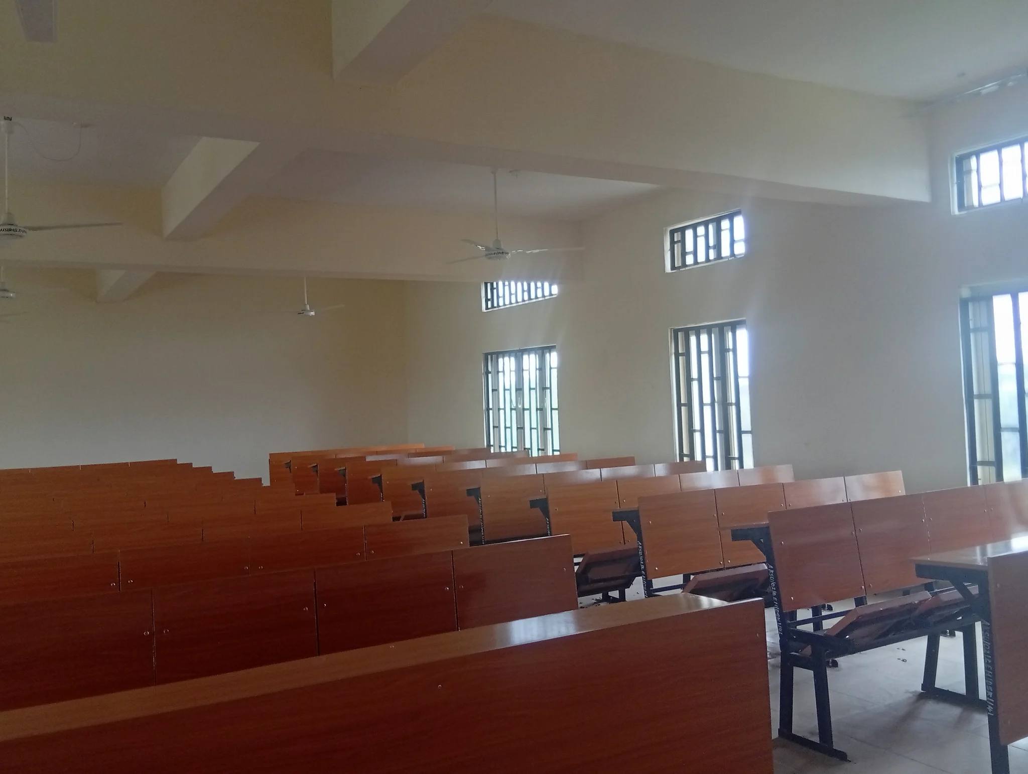 Rows of wooden desks and benches beside open windows in an empty classroom.
